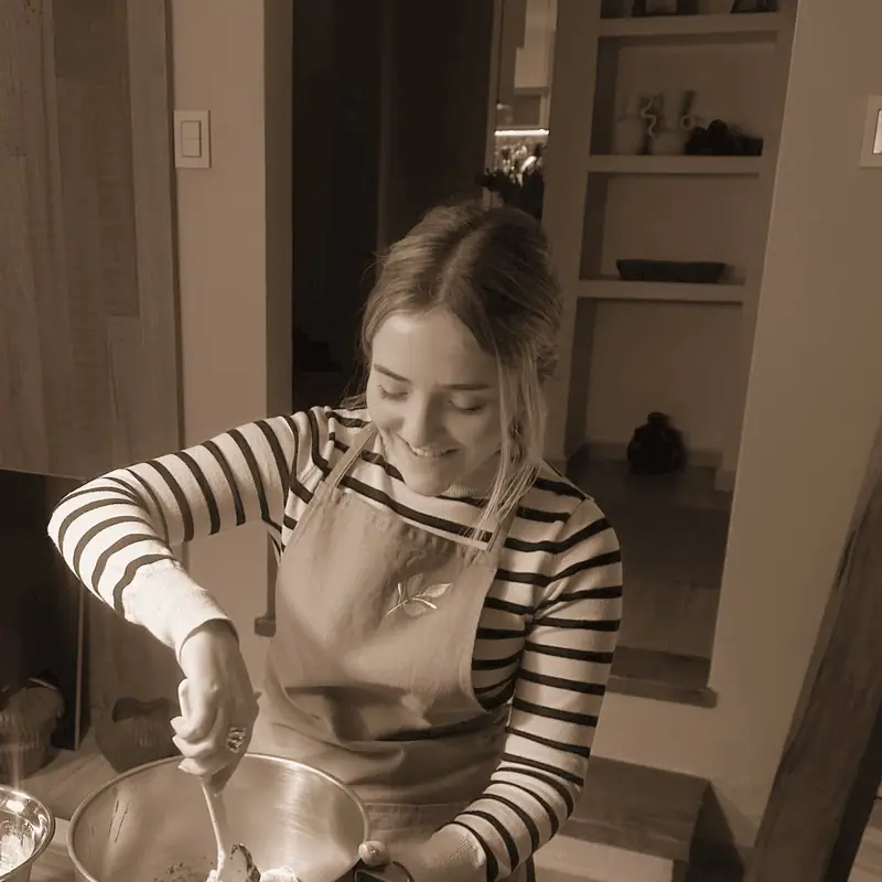 Pili sonriendo mientras bate en la cocina, con el delantal de Entre Nos